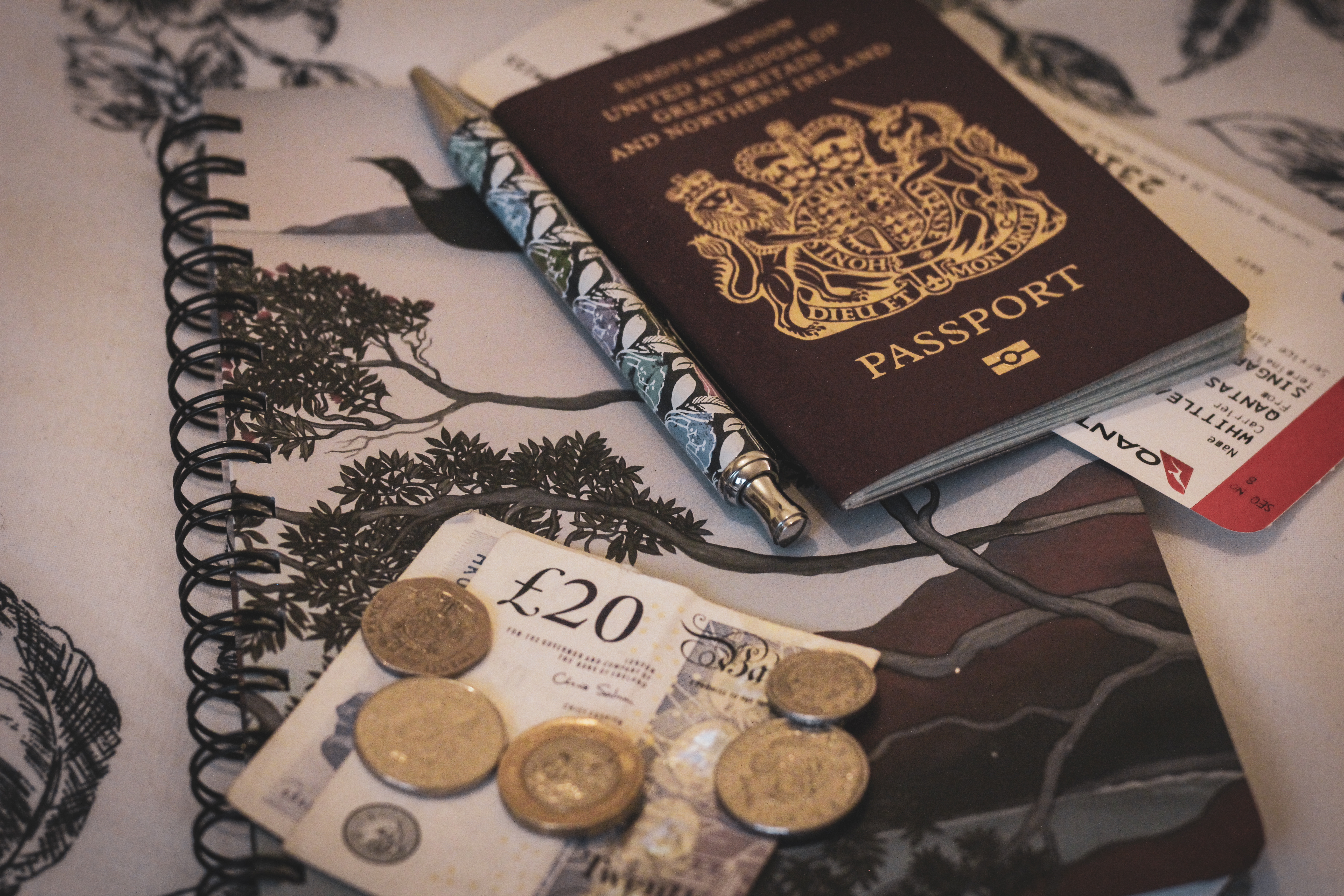 Cash and passport sit on top of a notebook with a pen