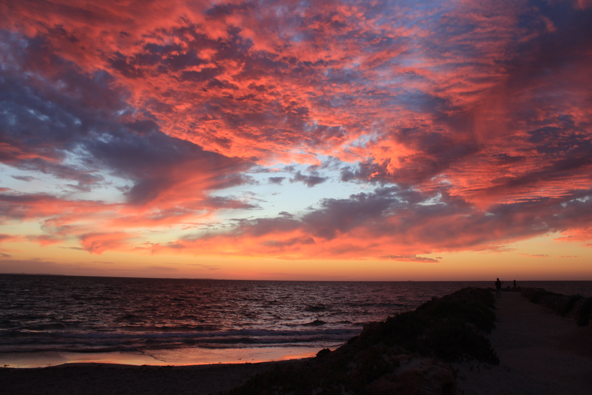 Bright pink and purple clouds of a sunset over the beach and sandy pier