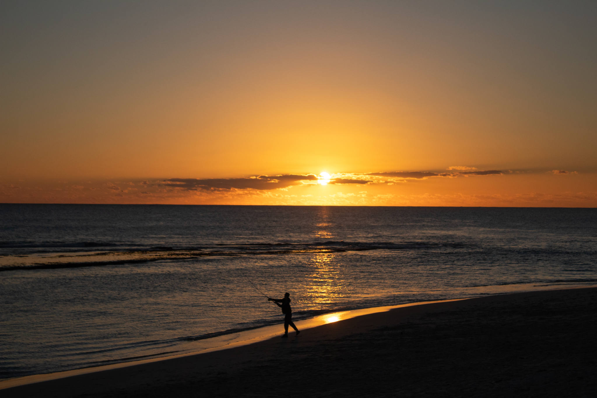 man throws fishing line into ocean at sunset over Yanchep